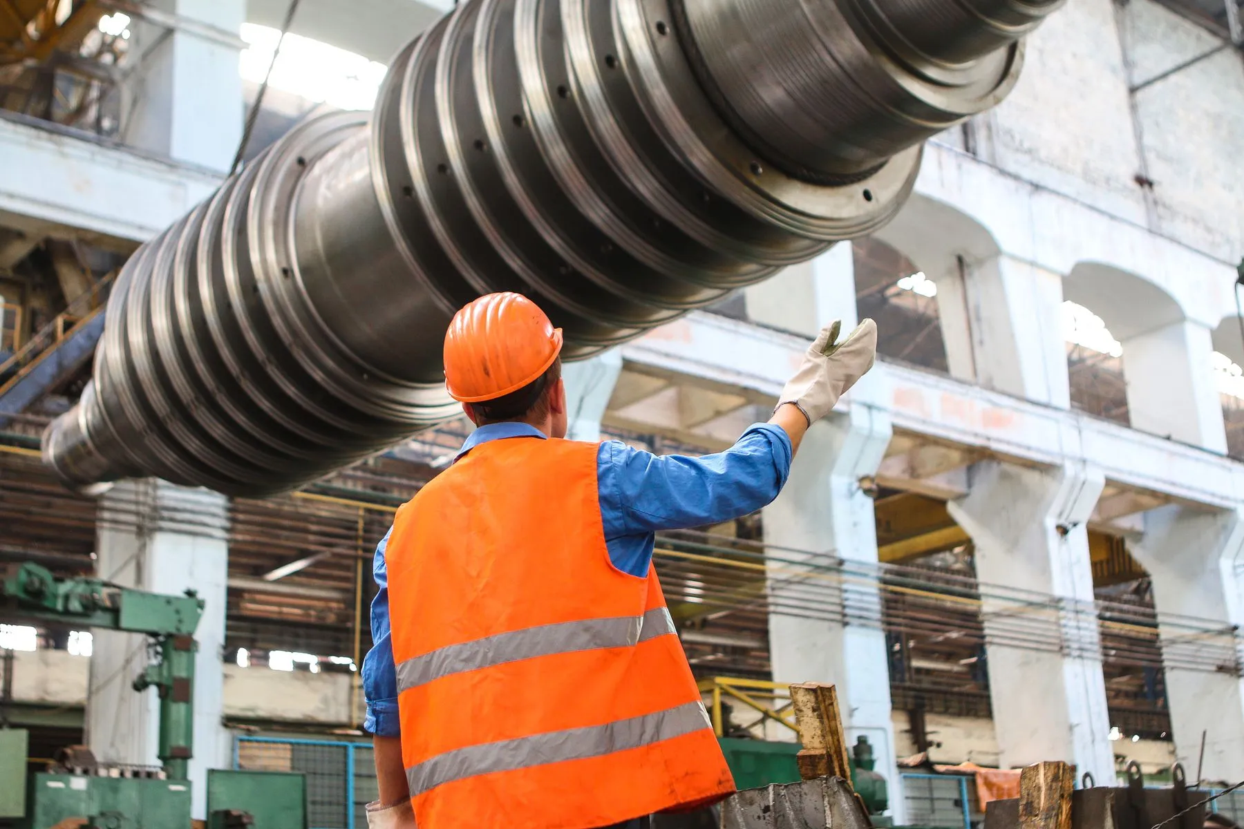 Engineer in a hard hat inspecting a large machined part on a factory floor